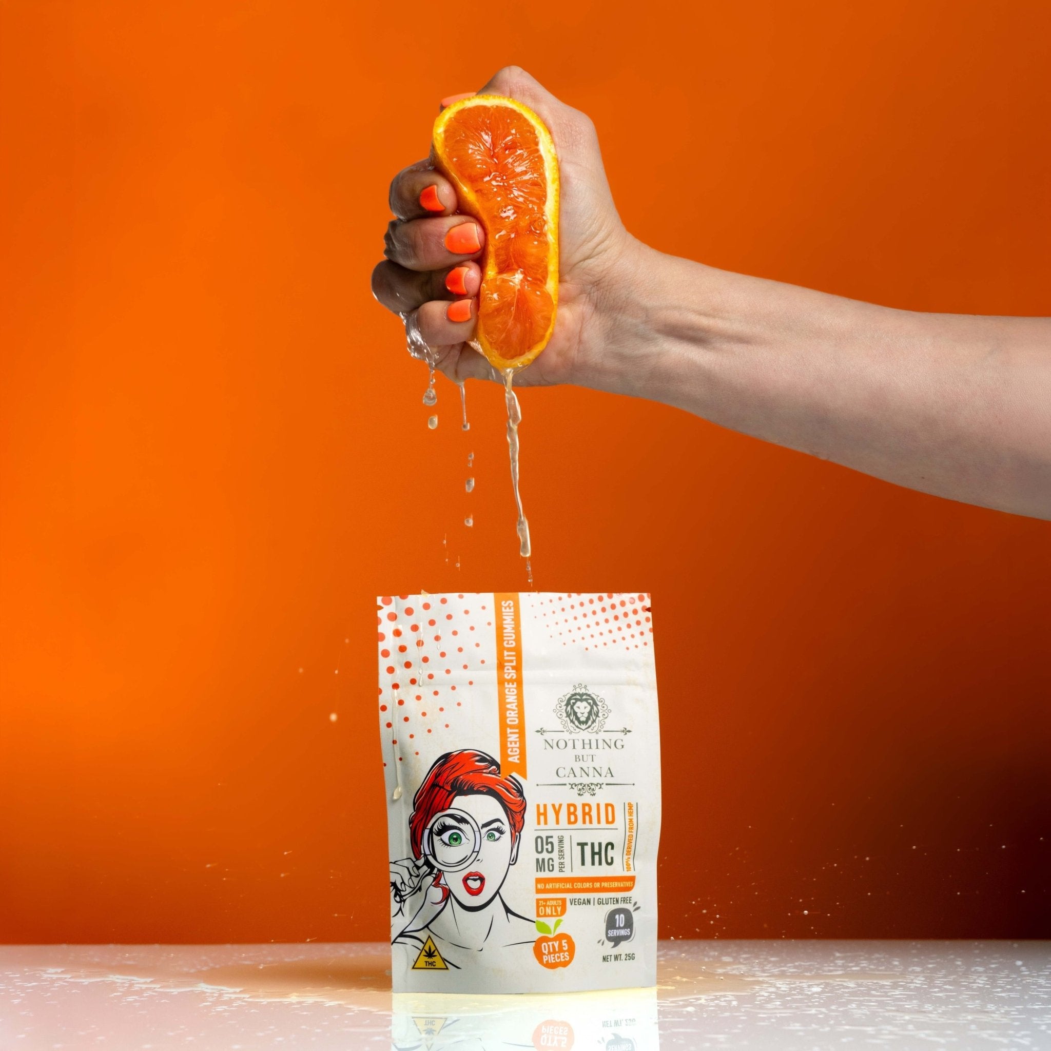 Nothing But Hemp Agent Orange hemp-derived delta-9 THC hybrid gummies bag on white table with orange background while a hand squeezes a fresh orange above the product to emphasize citrus theme