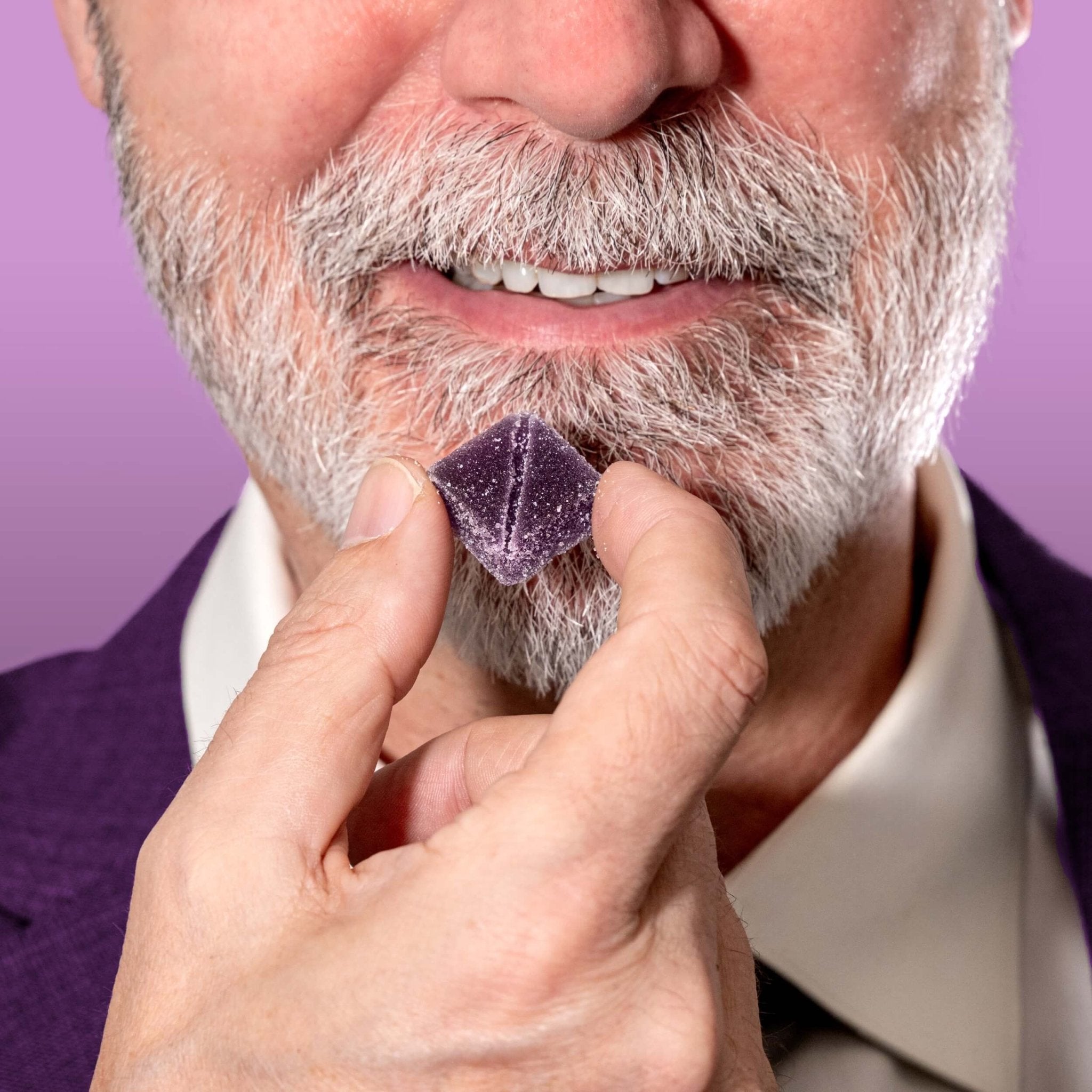 Nothing But Hemp Grand Daddy Purple hemp-derived THC and CBD indica gummies featuring model in purple suit holding a gummy up to his mouth about to take a bite while styled as a nod to the packaging character in a lifestyle cannabis setting